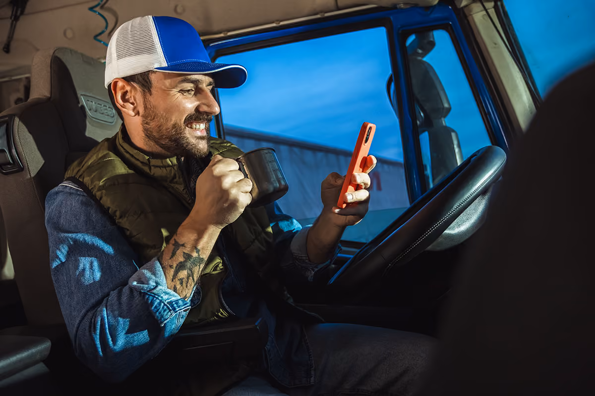 Tow truck driver drinking coffee while smiling at his phone
