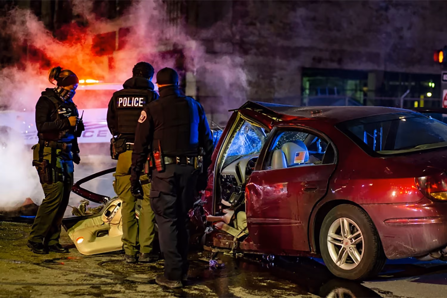 Bad car accident with police standing next to it and smoke pluming