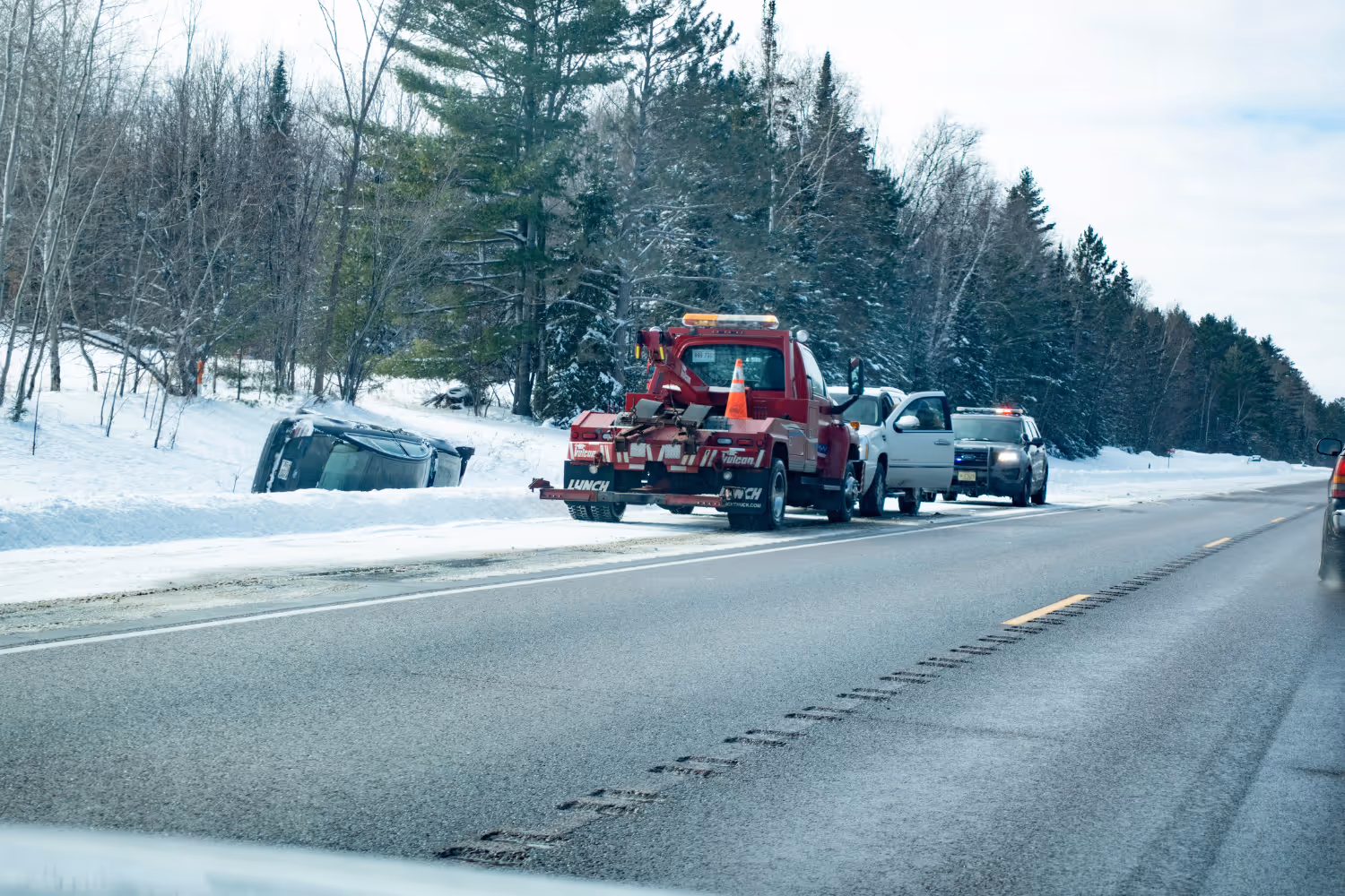 Tow truck on the side of the highway attending to a rolled over car in a winter landscape