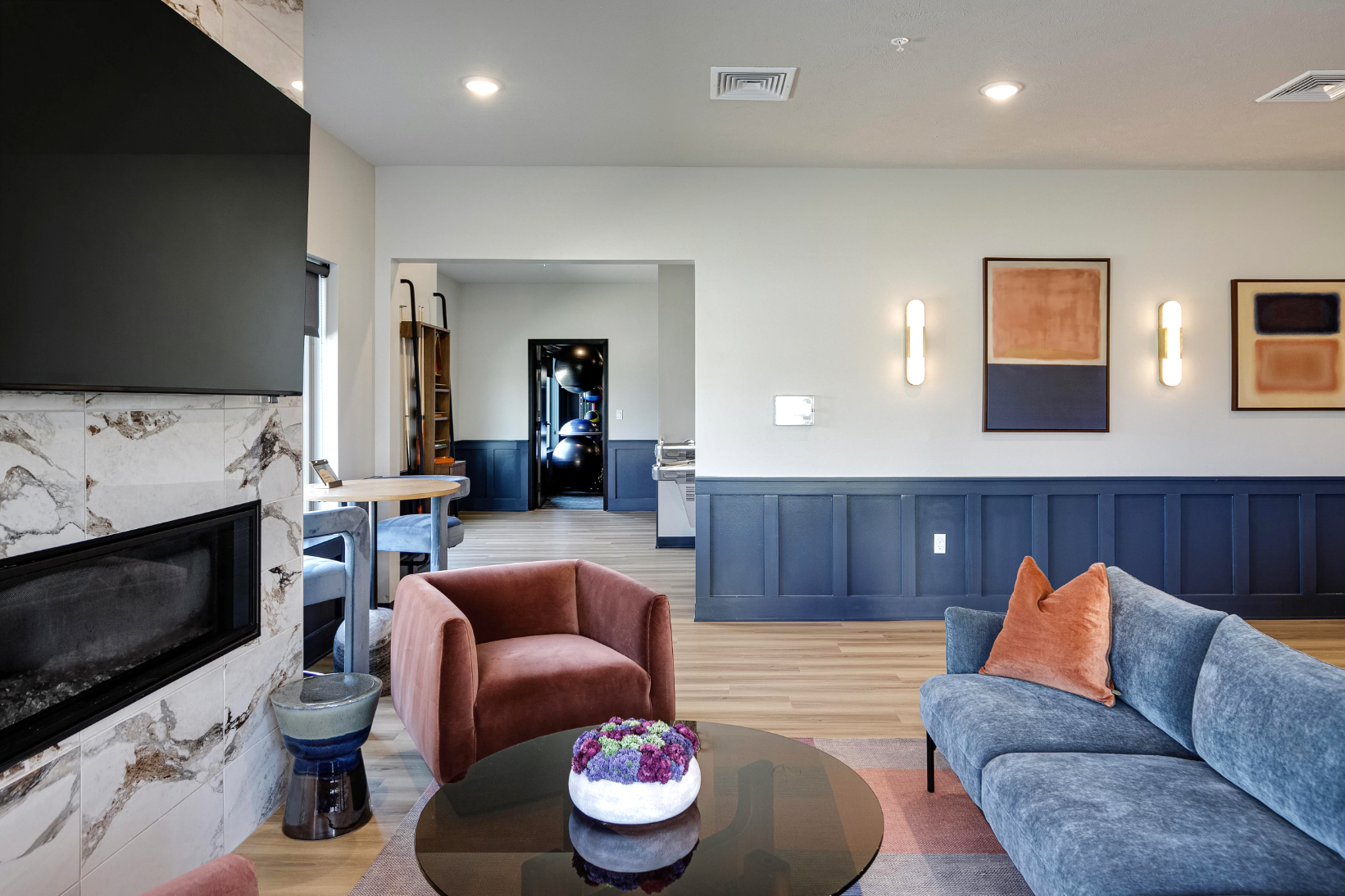 Clubhouse lounge area with tv and fireplace and view into gym