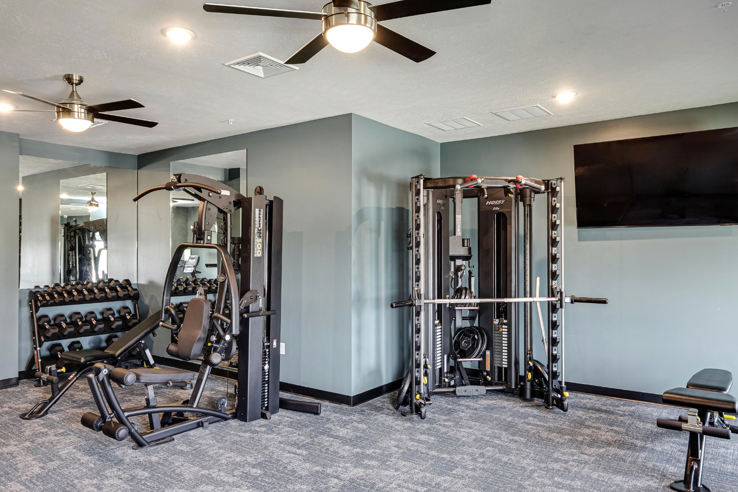 Clubhouse gym with fitness equipment featuring weight machine and dumbbells 