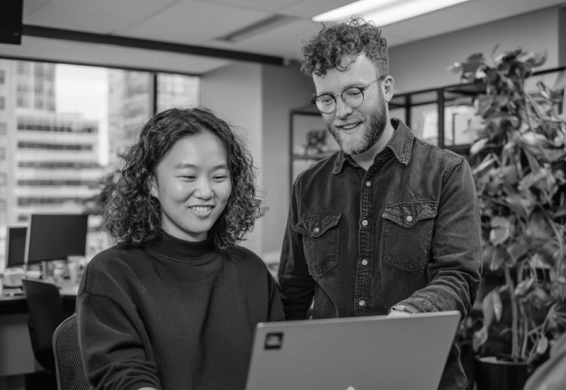 Coworkers Reviewing Project On Laptop In Open Office PromptEngine Webflow Template | BRIX Template