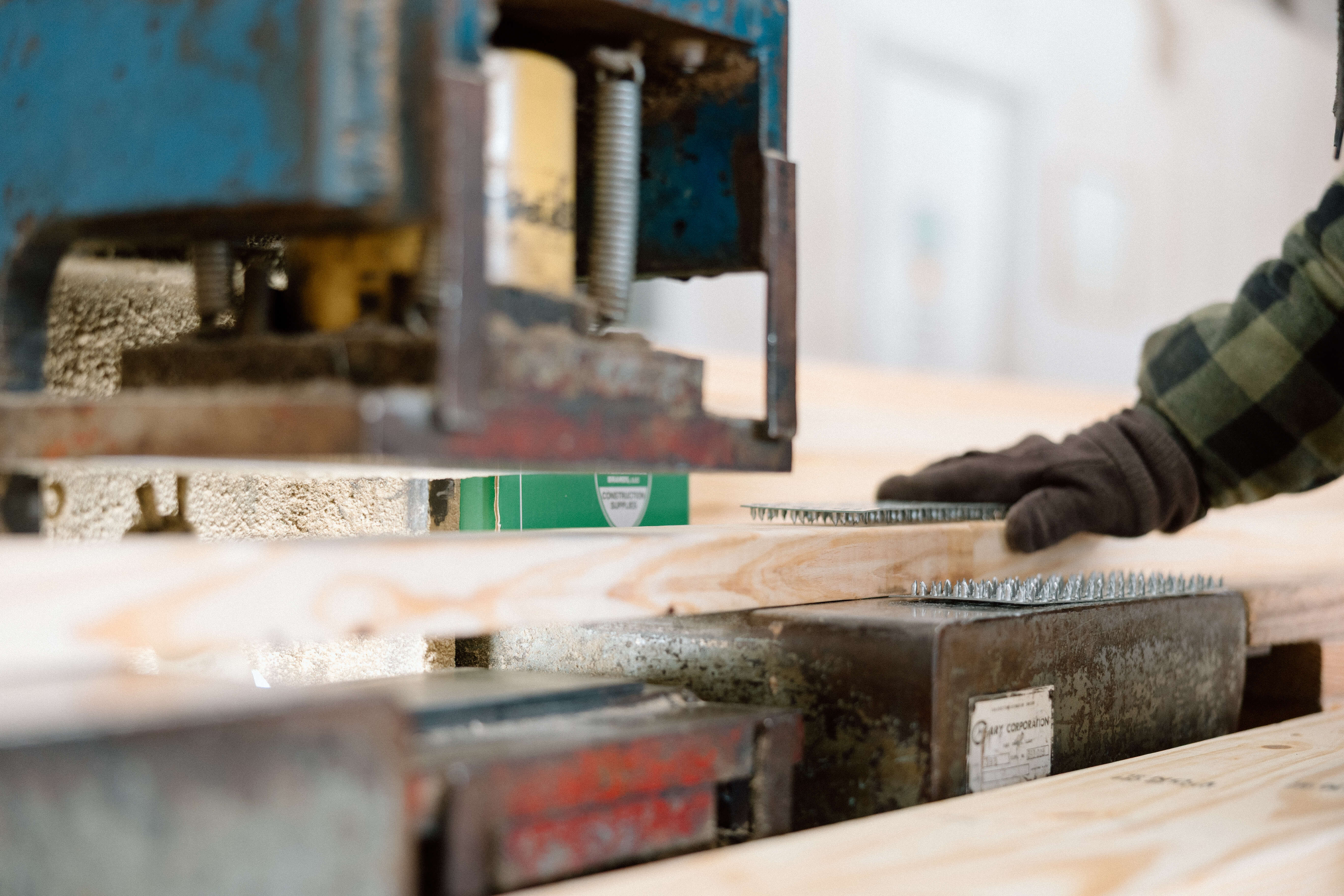 Close-up of a worker's gloved hand placing metal fasteners on wooden planks near industrial machinery.