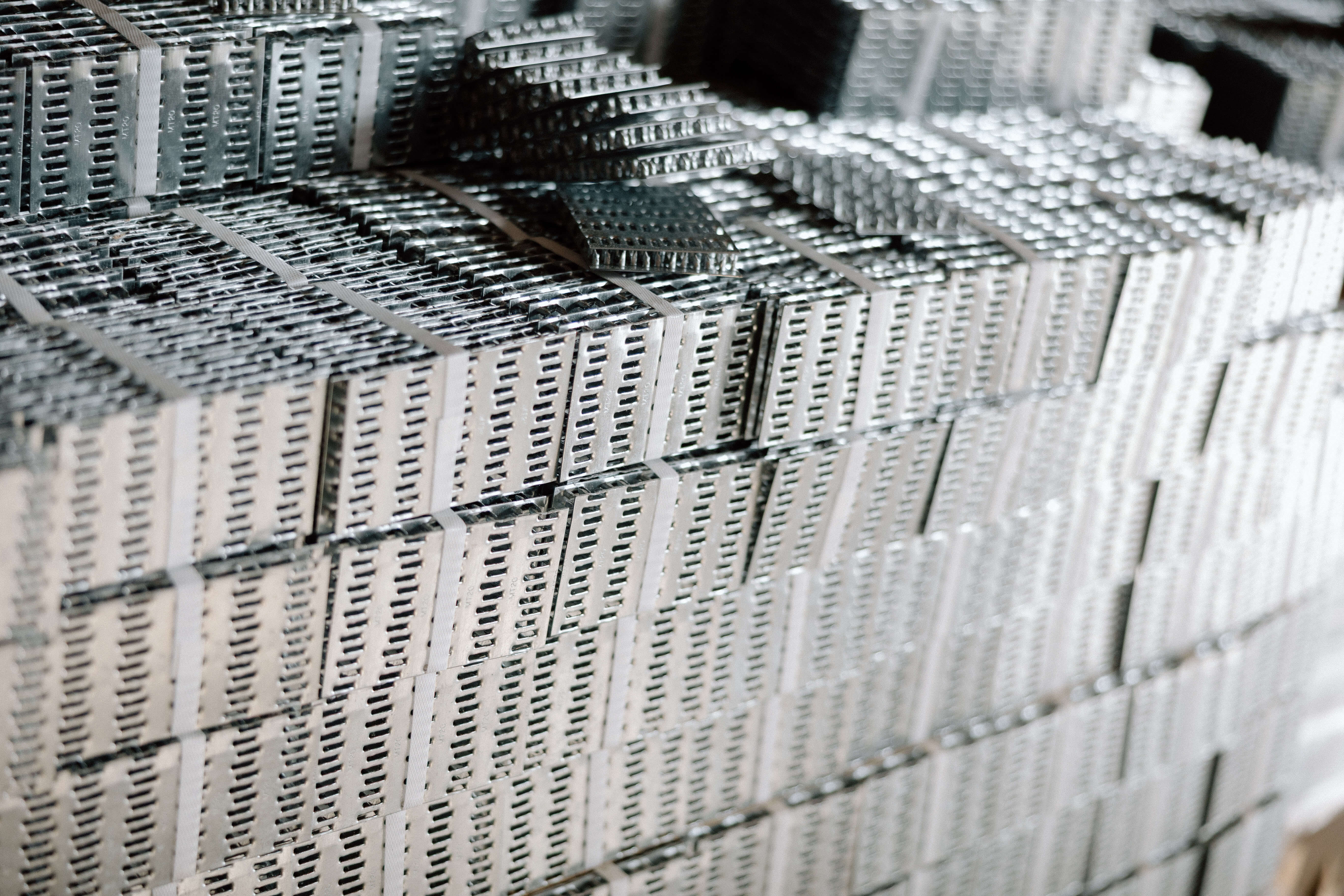 Stacks of silver metal truss plates bundled and arranged on factory shelves.