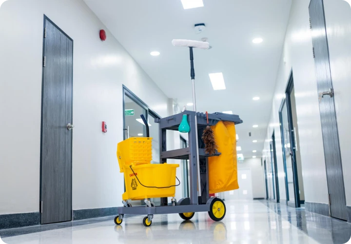 Janitor cart with yellow mop bucket and cleaning supplies in a clean, modern hallway.