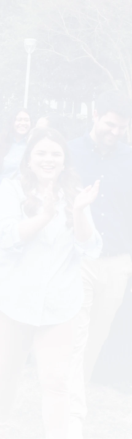 Group of young adults smiling and clapping outdoors near trees and a street lamp.