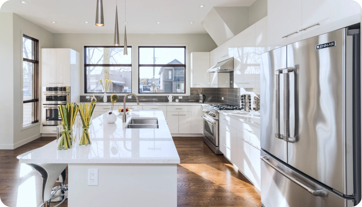 Bright modern kitchen with white cabinets, stainless steel appliances, large island with sink, and three pendant lights.