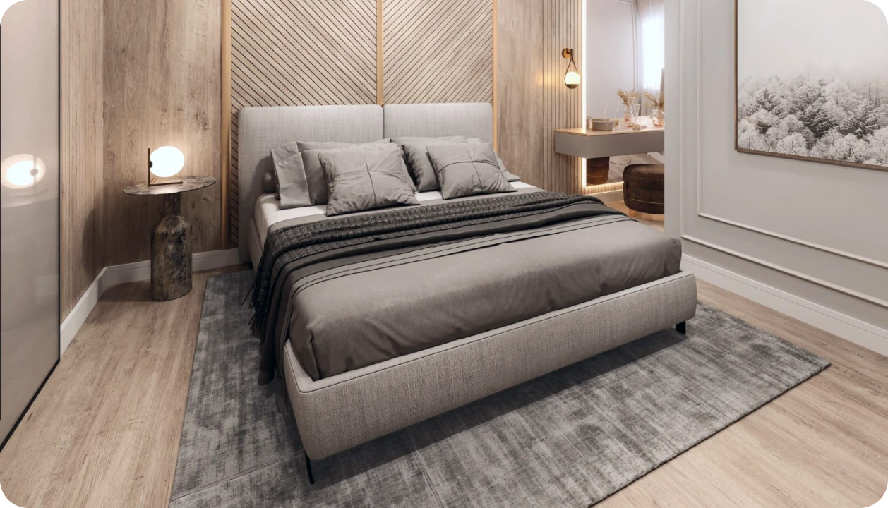 Modern bedroom with a large gray upholstered bed, gray bedding, wooden accent walls, a small round side table with a lamp, and a framed forest artwork on the wall.