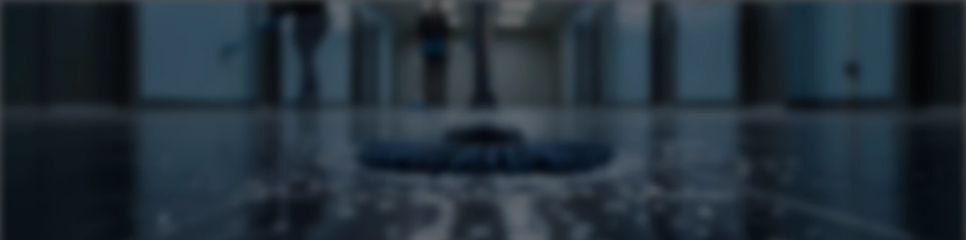 Floor cleaning machine scrubbing a shiny tiled floor in a commercial building lobby.