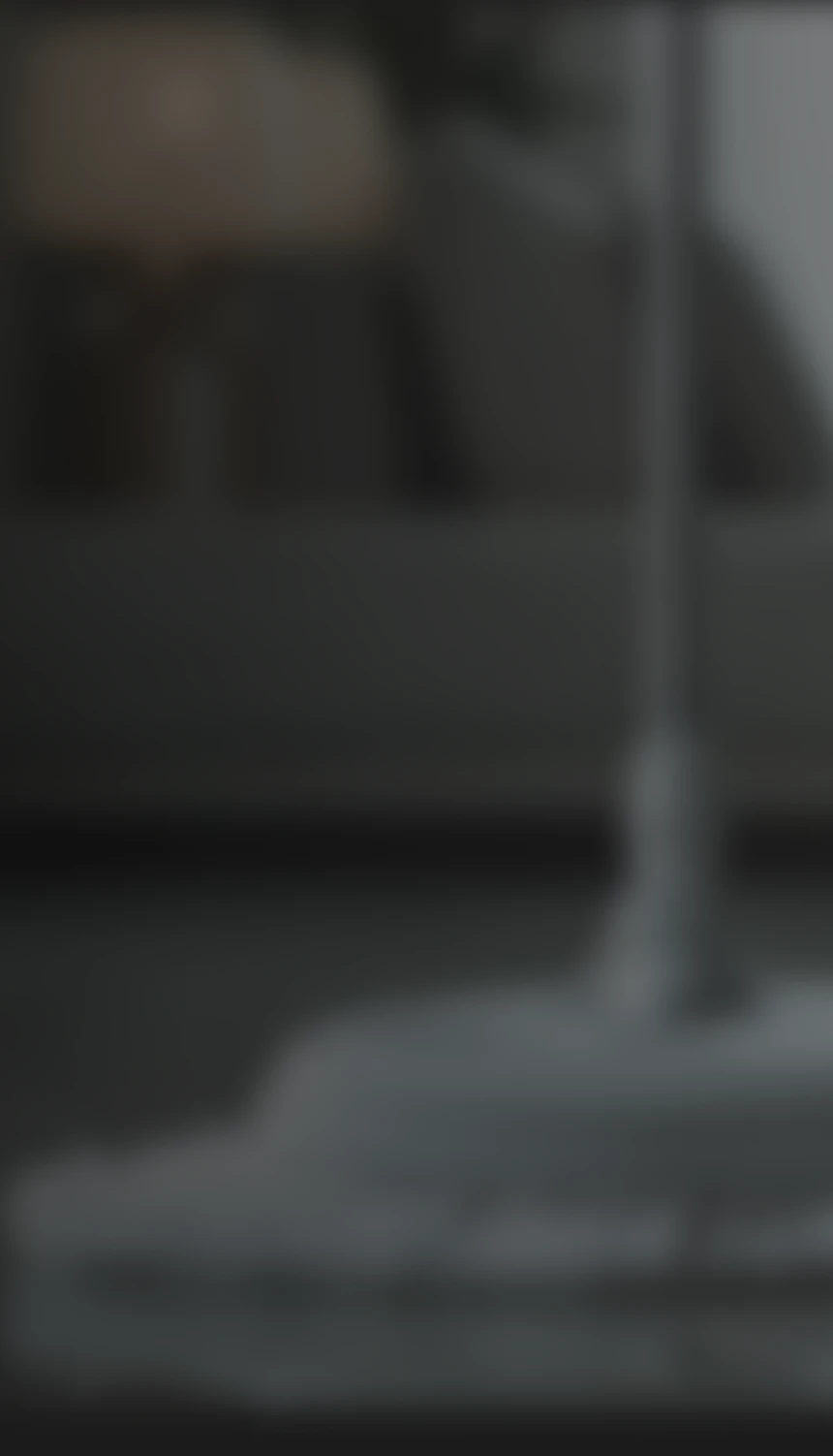 Blurred image showing a room interior with a sofa and a tall floor lamp in the foreground.