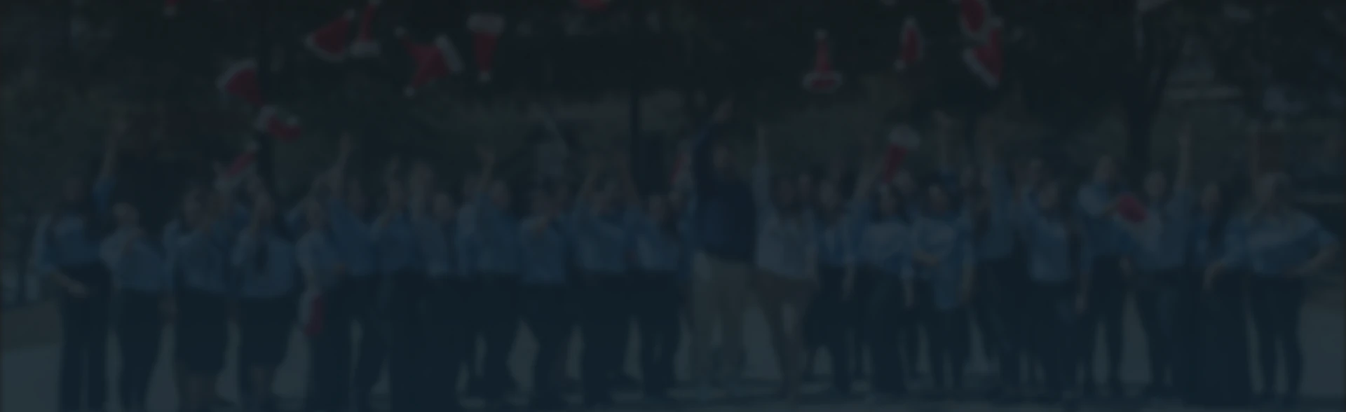 Group of people outdoors wearing blue shirts tossing red Santa hats into the air in celebration.