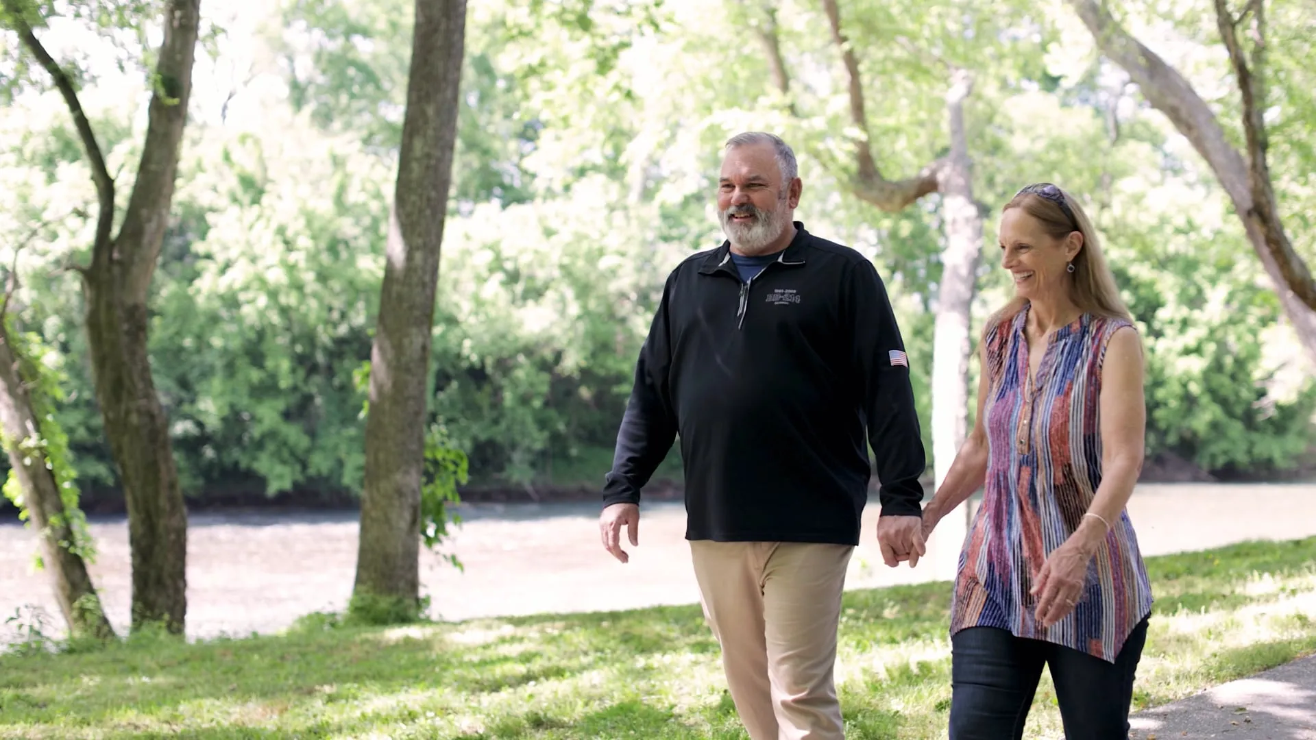 A man and woman are walking hand in hand in a park, smiling.
