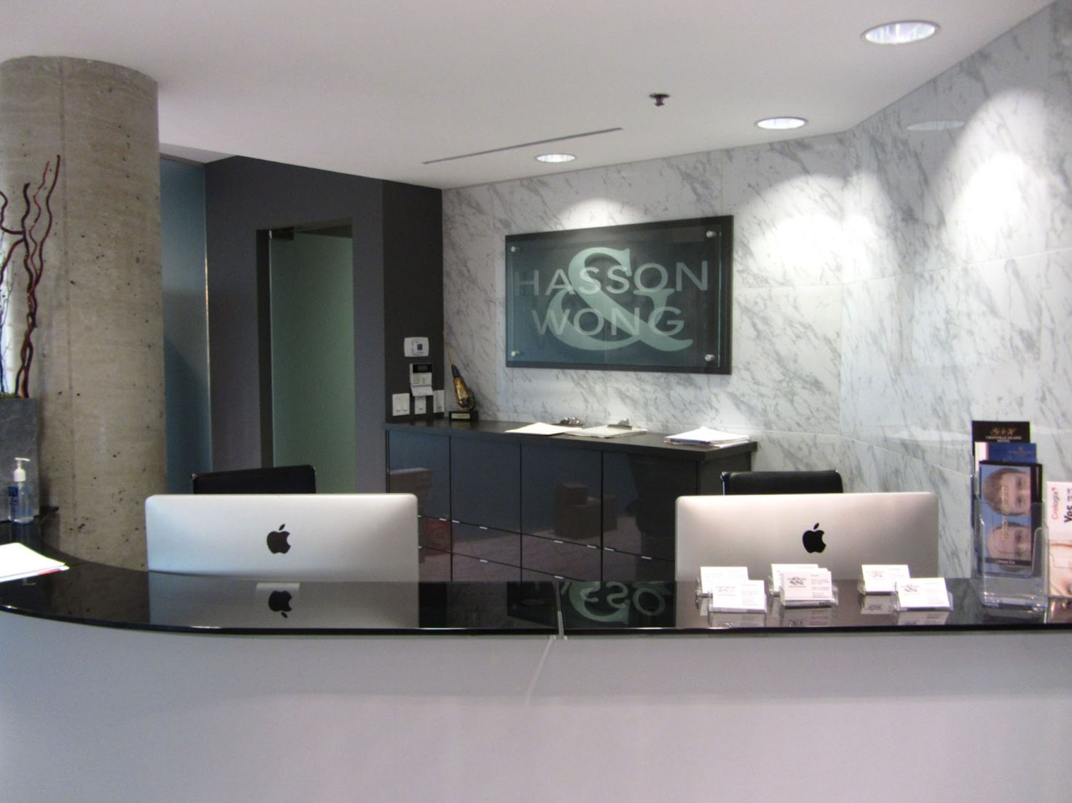 A modern office reception area with two computers on a curved desk, and a sign reading "Hasson & Wong."