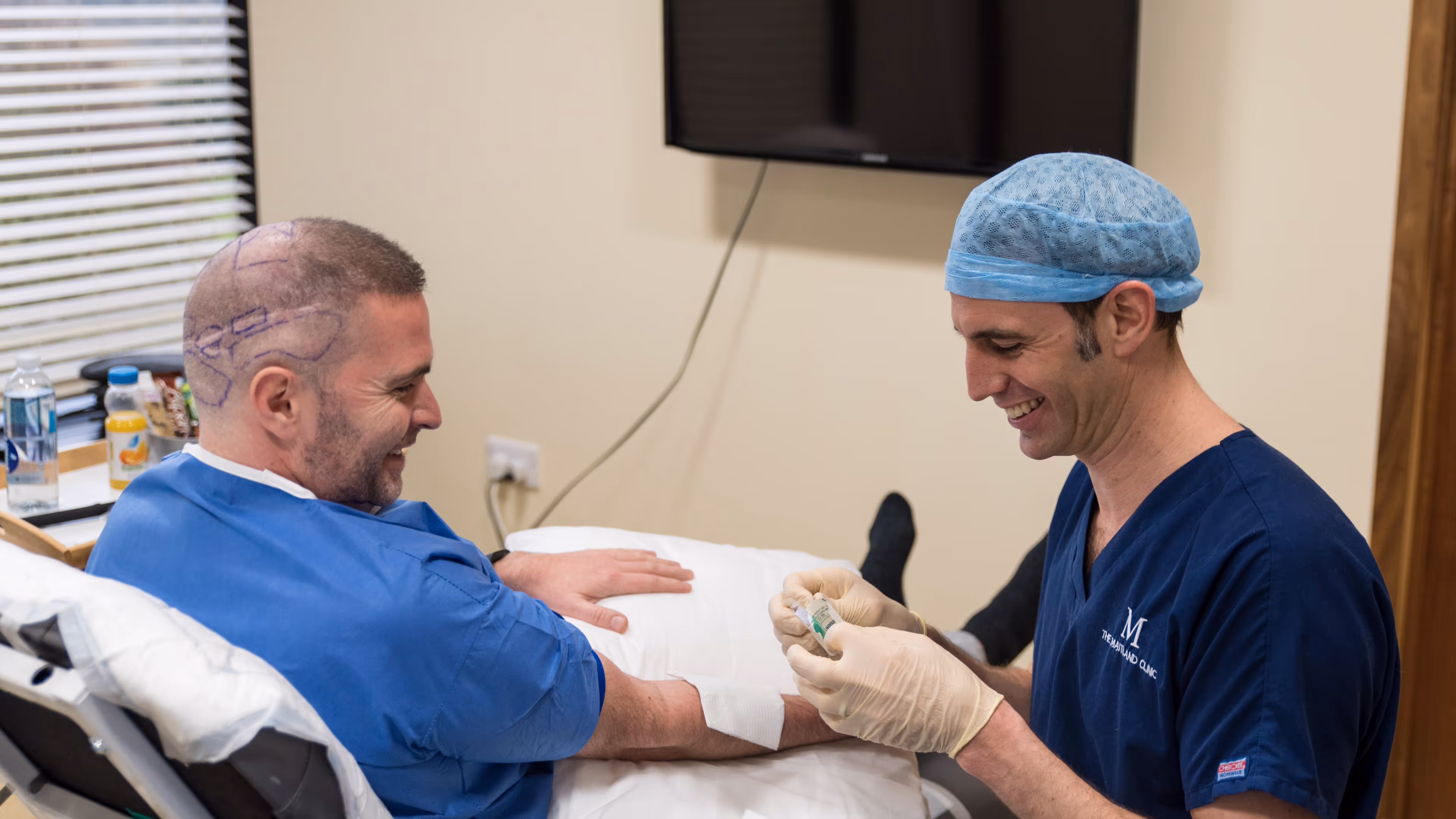 A doctor prepares a man's arm for a procedure while he sits in a medical chair.