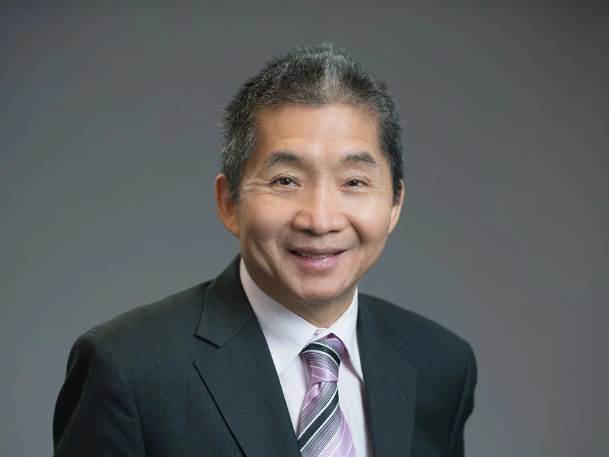 A person in a suit and tie smiles against a plain background.