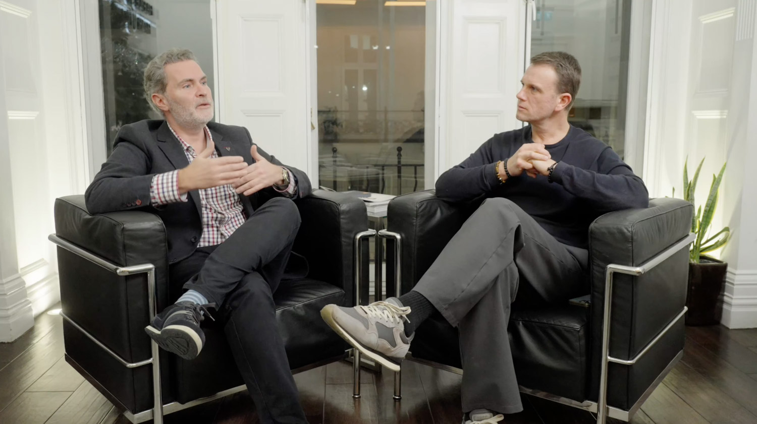 Two men seated in chairs having a discussion in a bright room.