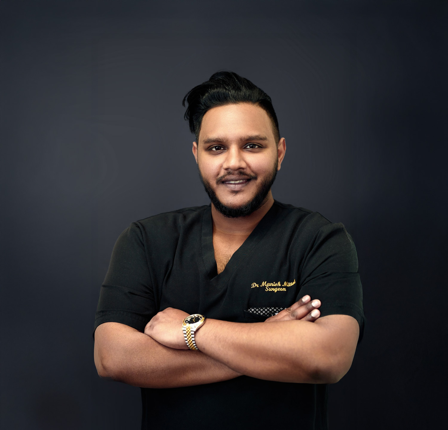 A man in a black shirt stands with arms crossed, smiling at the camera.