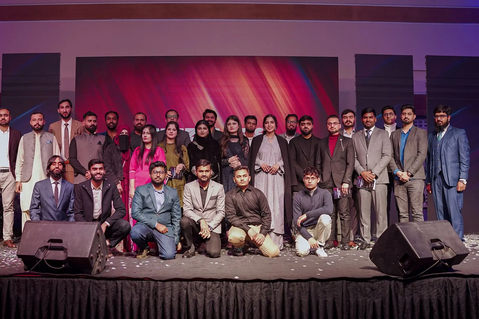 A group of individuals standing on stage, smiling and posing for a photo, with bright lights illuminating the scene.