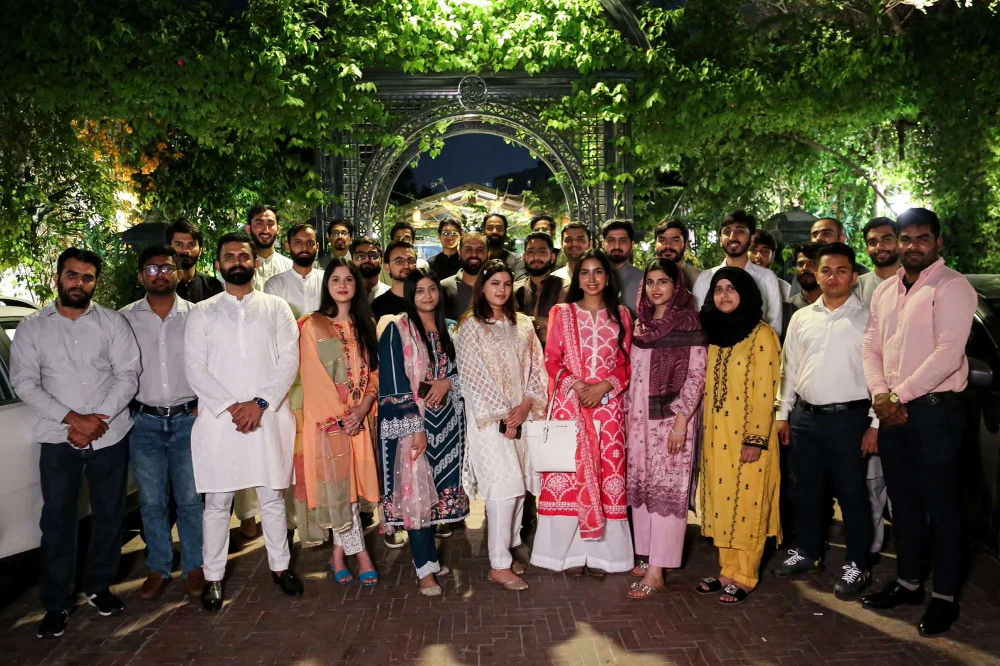  A cheerful group of people poses for a photo, surrounded by a beautiful garden filled with various flowers and greenery.