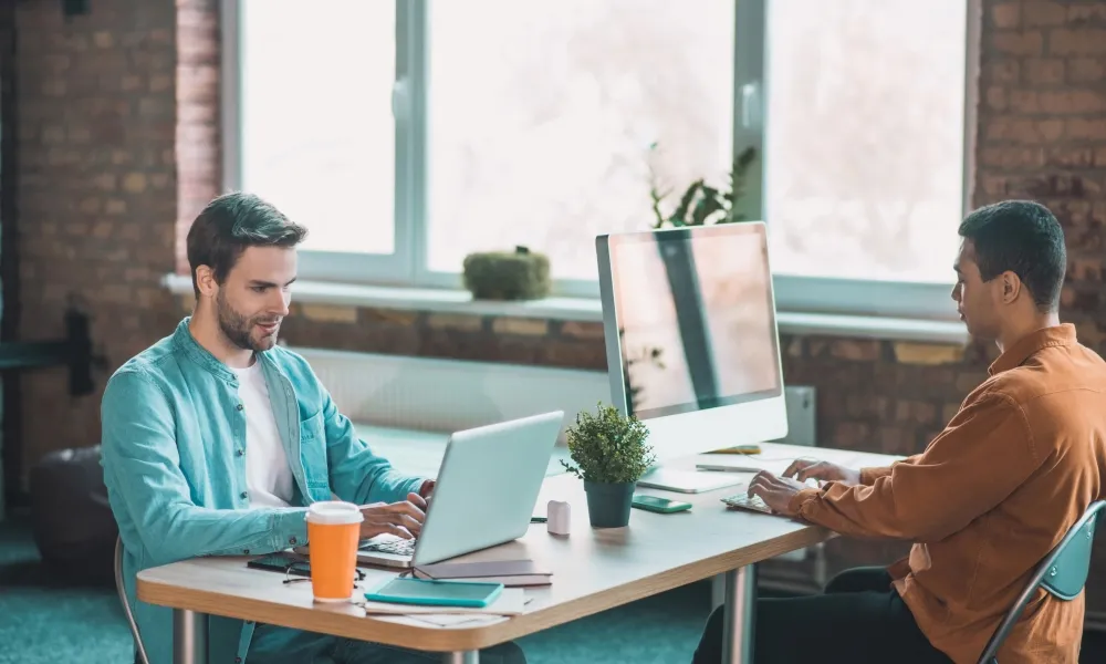 Two men at a table with laptops, collaborating on AI-powered gamification for corporate training in the energy sector.