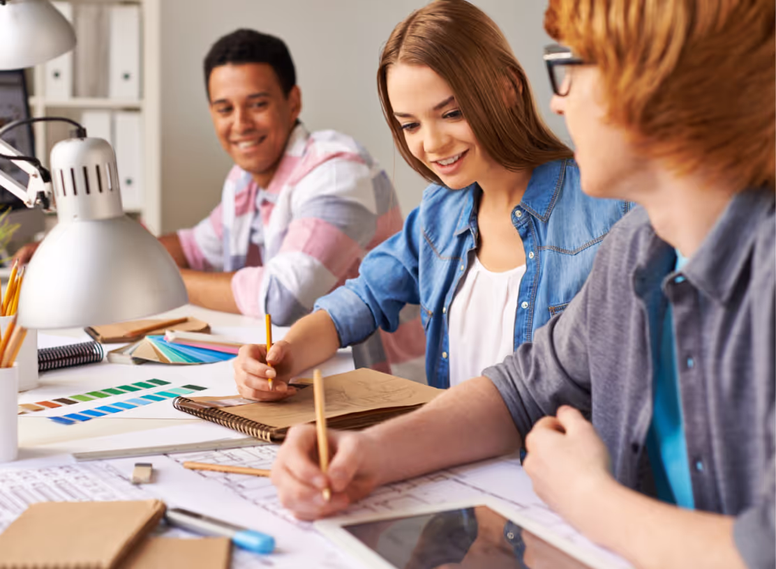 hree young individuals collaborate at a table, engaging with a laptop and papers, focused on their project.
