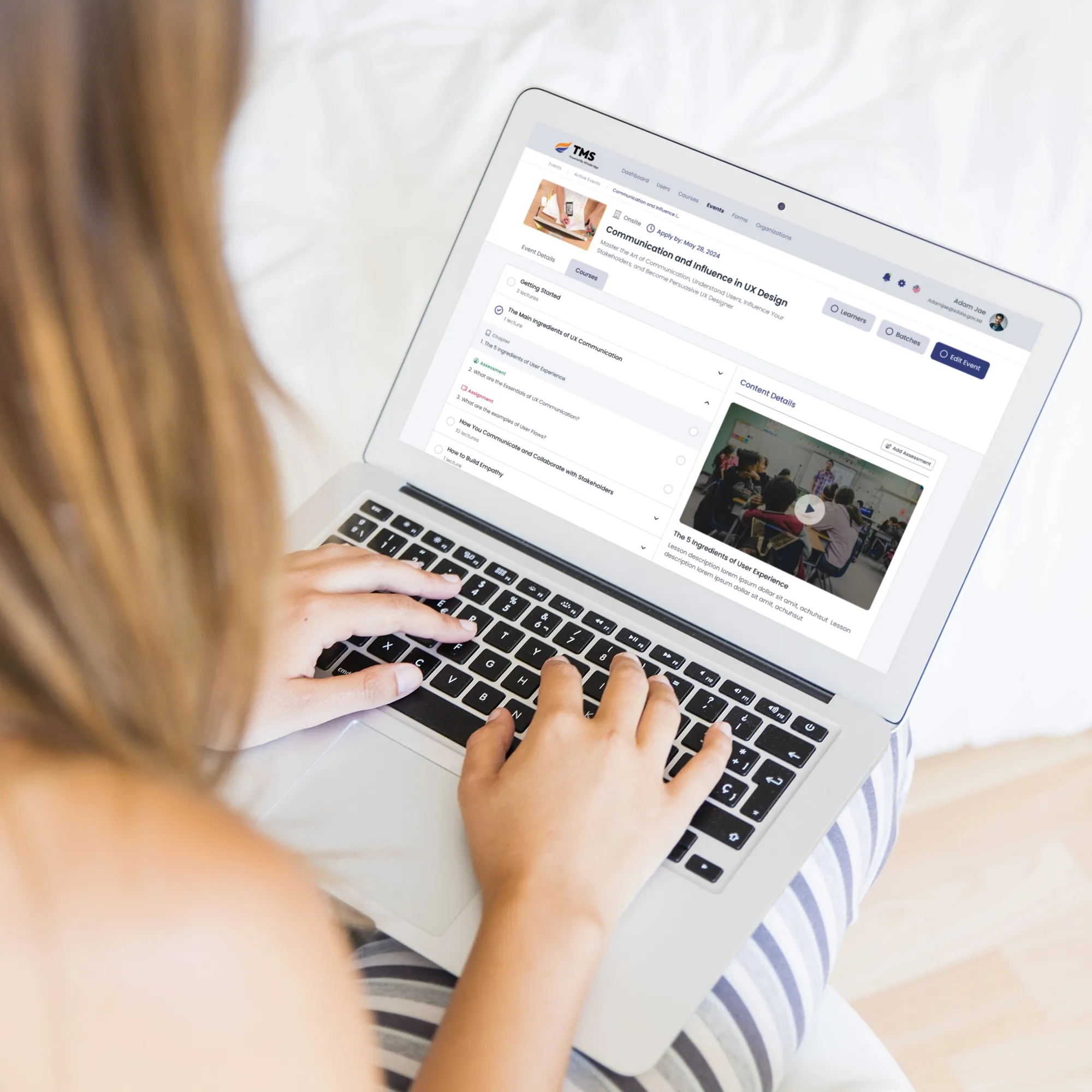 A woman types on her laptop while seated on a bed, engaged in her tasks in a comfortable setting.