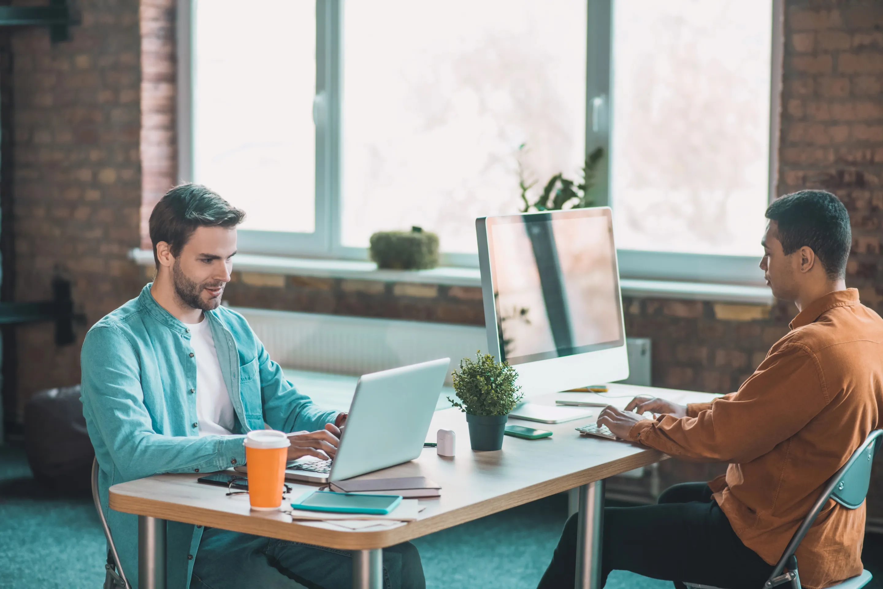 Two men at a table using laptops, discussing AI-driven training solutions in an educational technology setting.