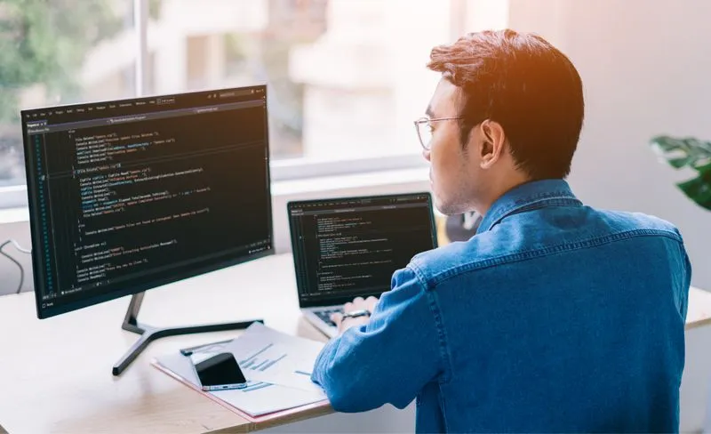 A man seated at a desk with two computers, working on generative AI solutions for software development productivity.
