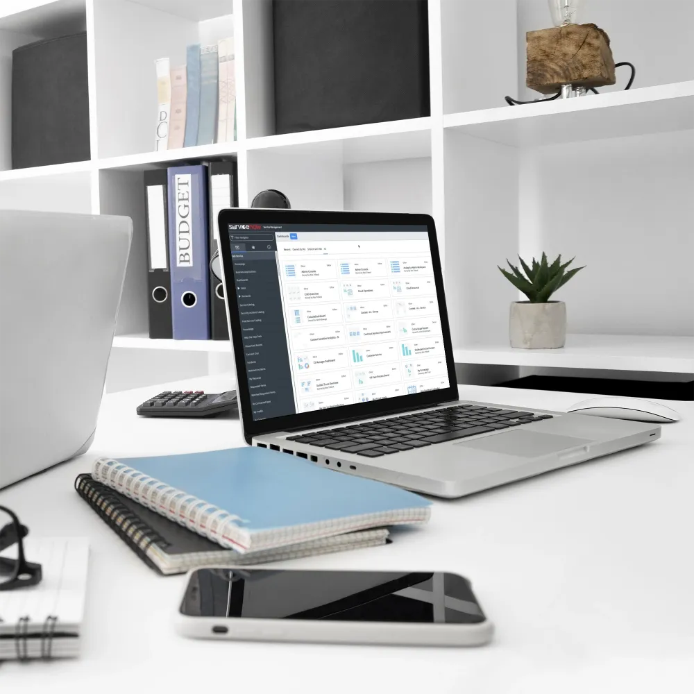 A laptop, notebook, and phone arranged neatly on a desk, symbolizing a modern workspace for IT service management.