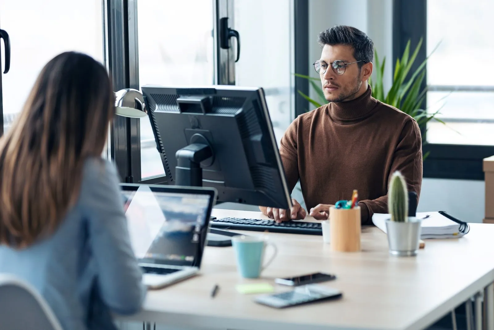 A man and woman collaborate at a desk with a computer, focusing on Salesforce CPQ implementation for sales optimization.
