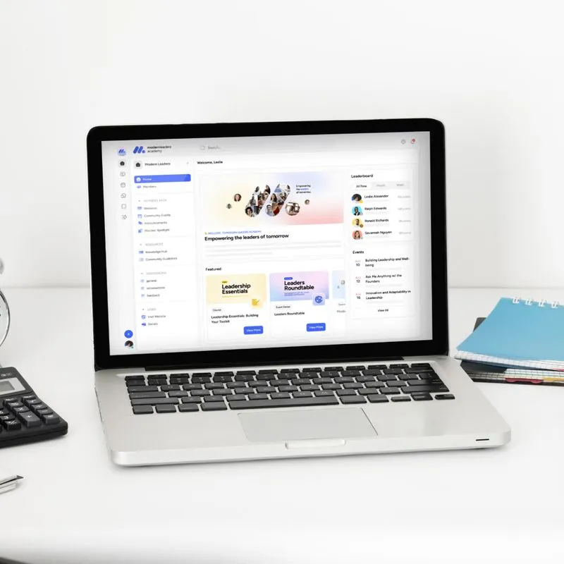 Laptop displaying a modern AI-powered training dashboard on a clean white desk with a calculator and notebooks nearby.