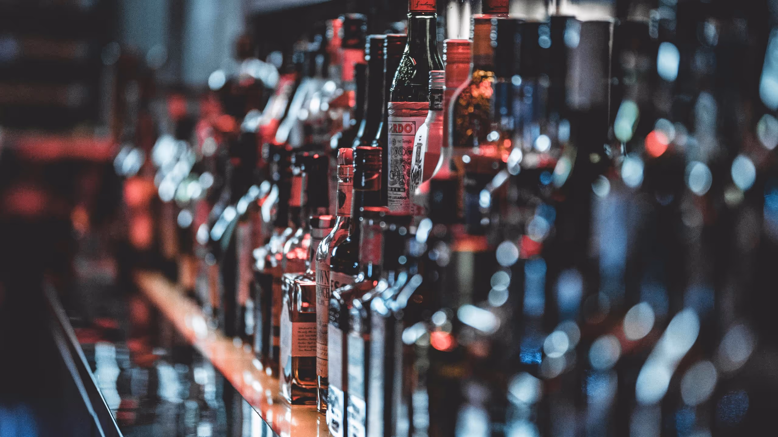 Rows of assorted liquor bottles lined up on a bar counter with a moody, blurred background.