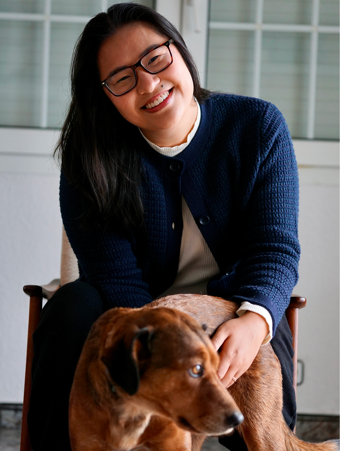 A photo of Andreanne smiling in a chair with her dog.