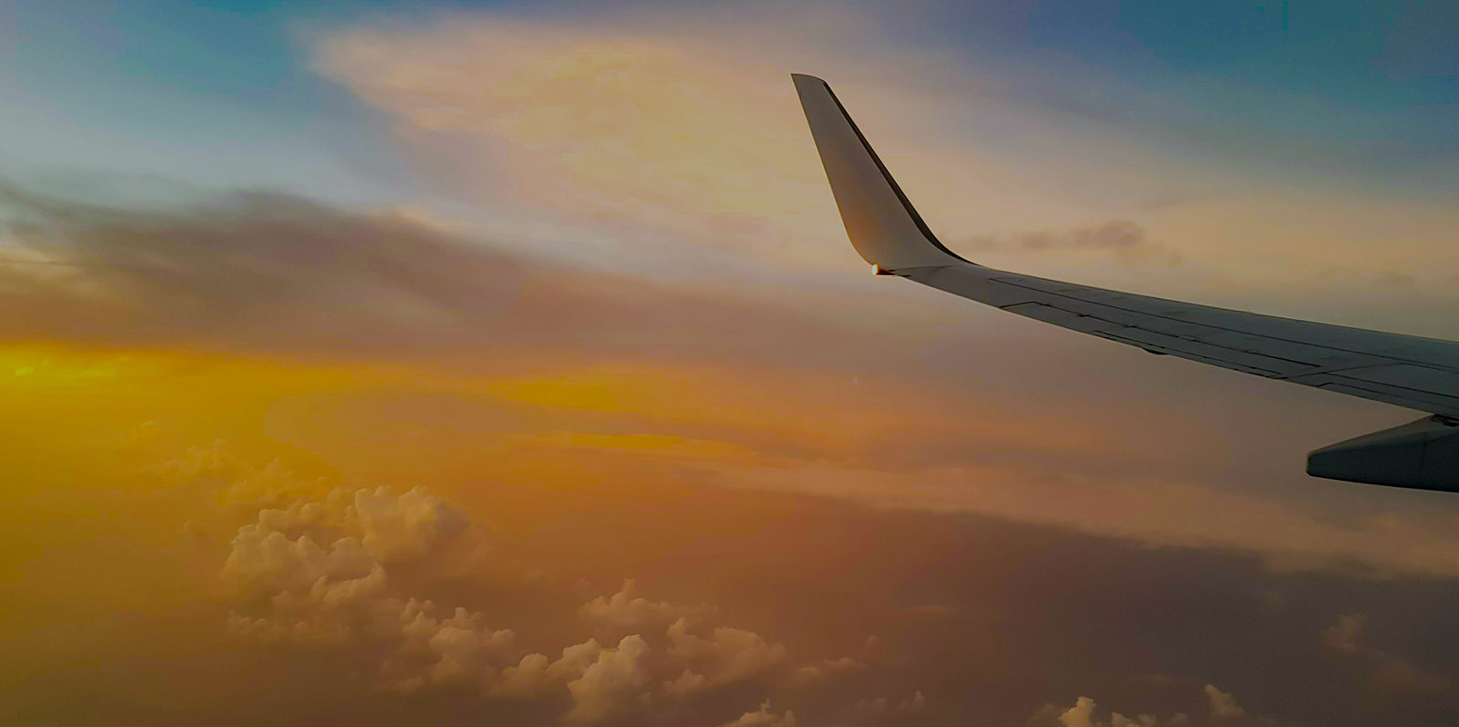 Airplane wing in flight against a sky with a colorful sunset and clouds below.
