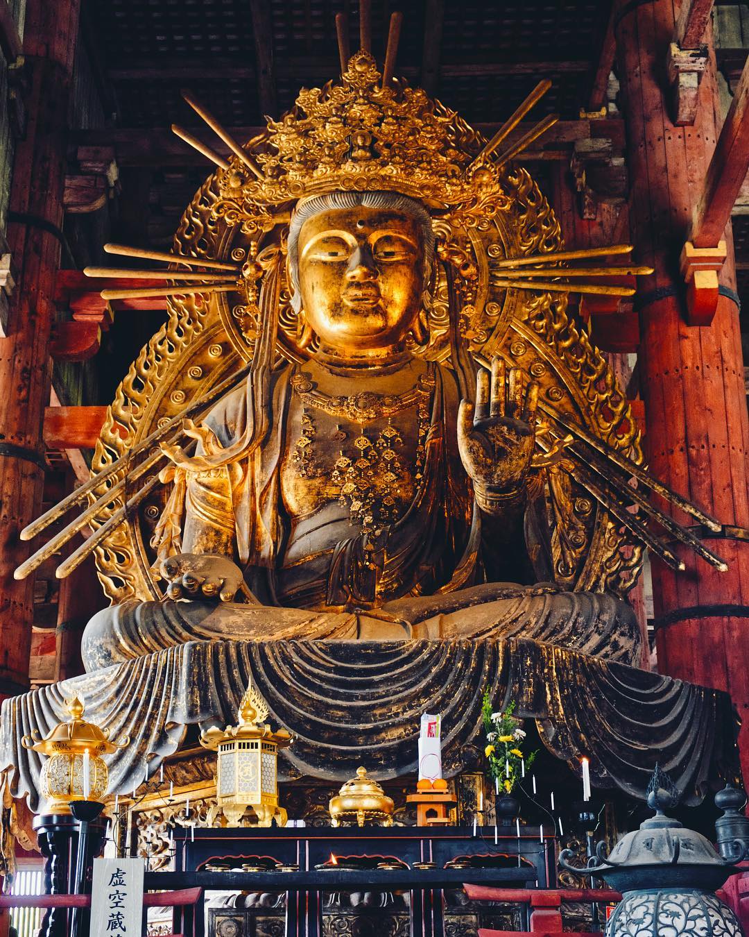 Golden Buddha statue seated in meditation with a detailed ornate halo and offerings in front inside a wooden temple.