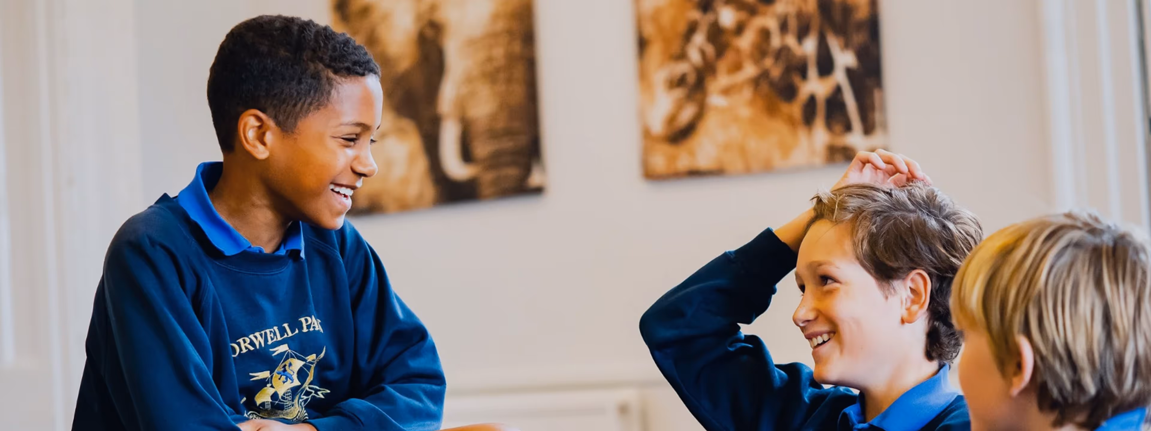 Three schoolboys smiling and chatting indoors, wearing blue uniforms.