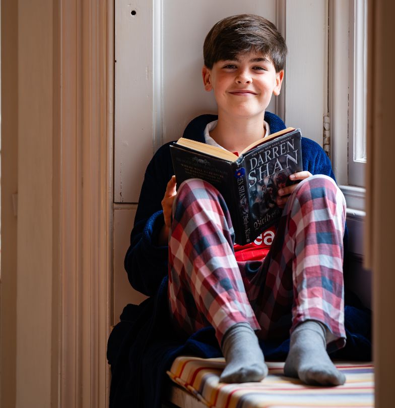 boy boarder reading a book in his dressing gown in the boys boarding house