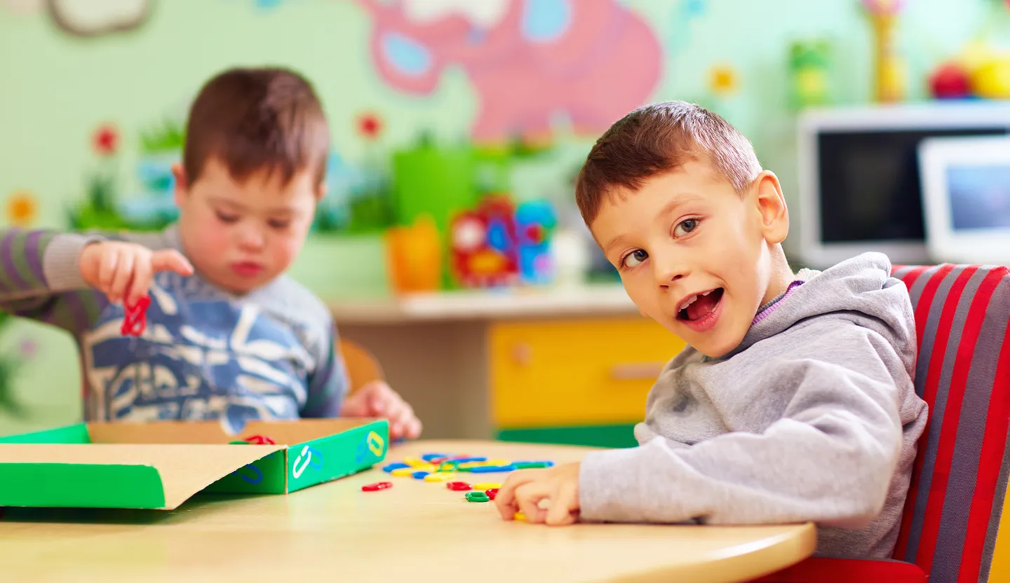 Two young boys playing with colorful plastic links at a table in a classroom.