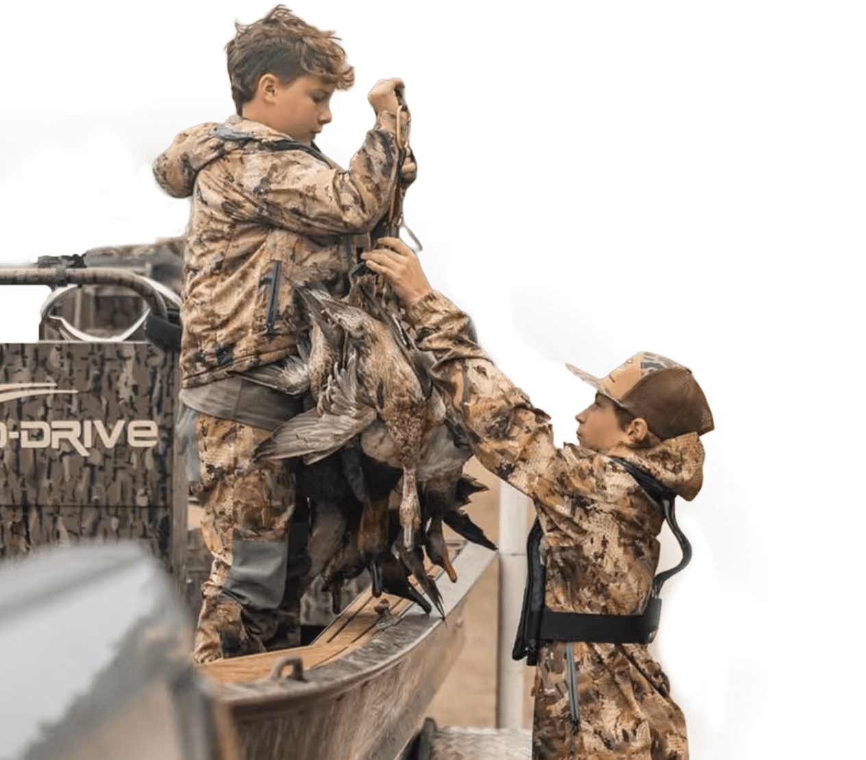 Two boys wearing camo hunting gear holding a bundle of ducks on a boat.