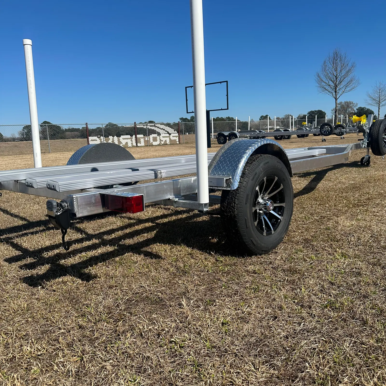Metal boat trailer with black wheels parked on dry grass under clear blue sky.
