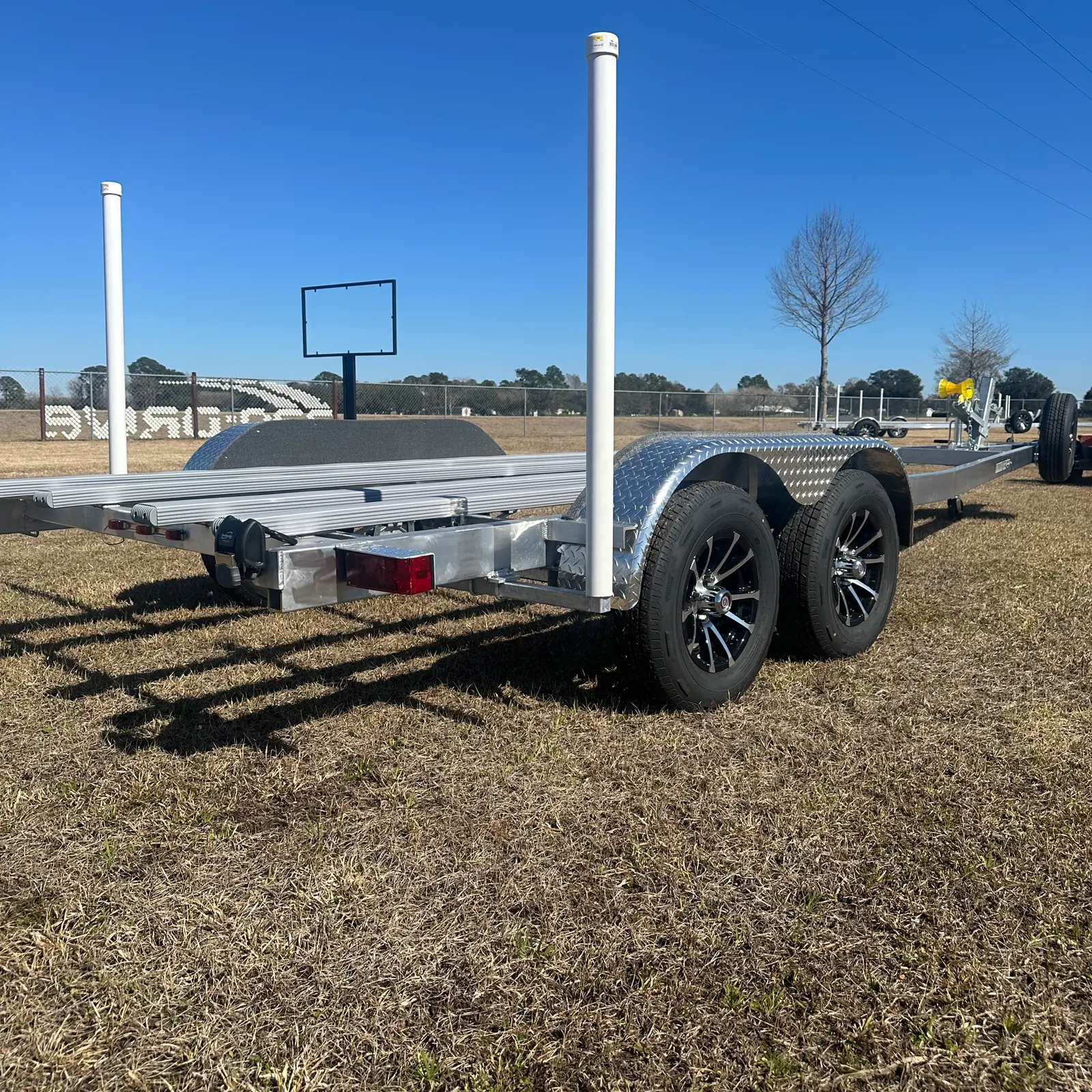 Metal trailer with dual wheels parked on dry grass under a clear blue sky.