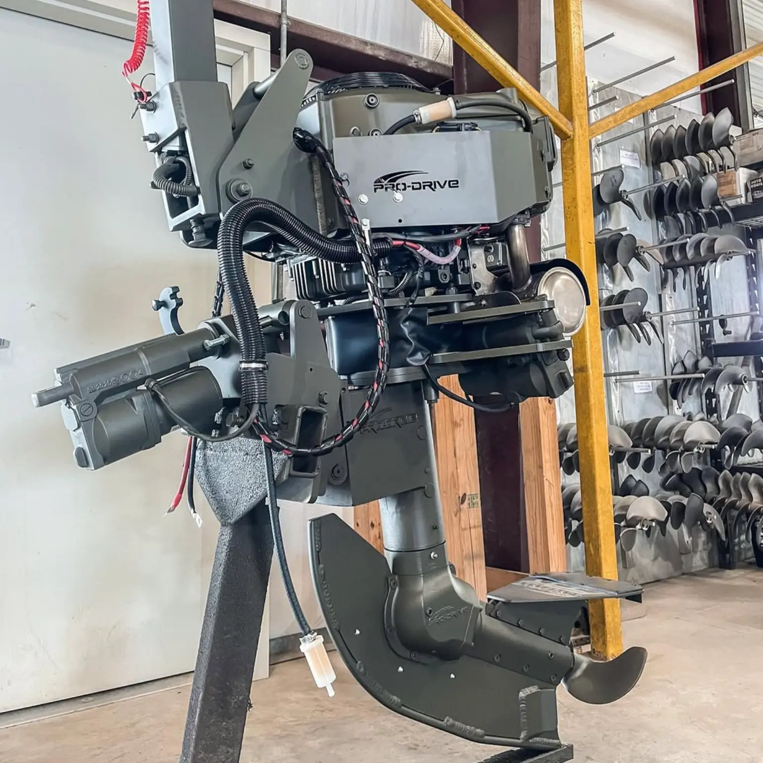 Gray Pro-Drive outboard motor displayed indoors with multiple propeller blades mounted on a wall in the background.