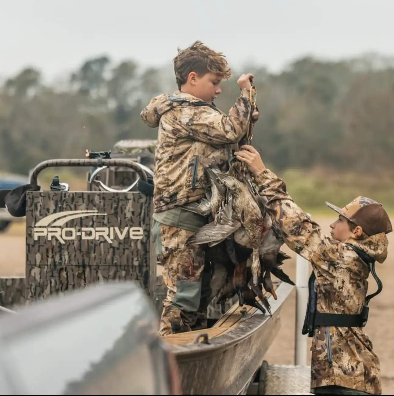 Two boys in camouflage clothing handling a string of hunted ducks on a boat with a camouflaged Pro-Drive motor.