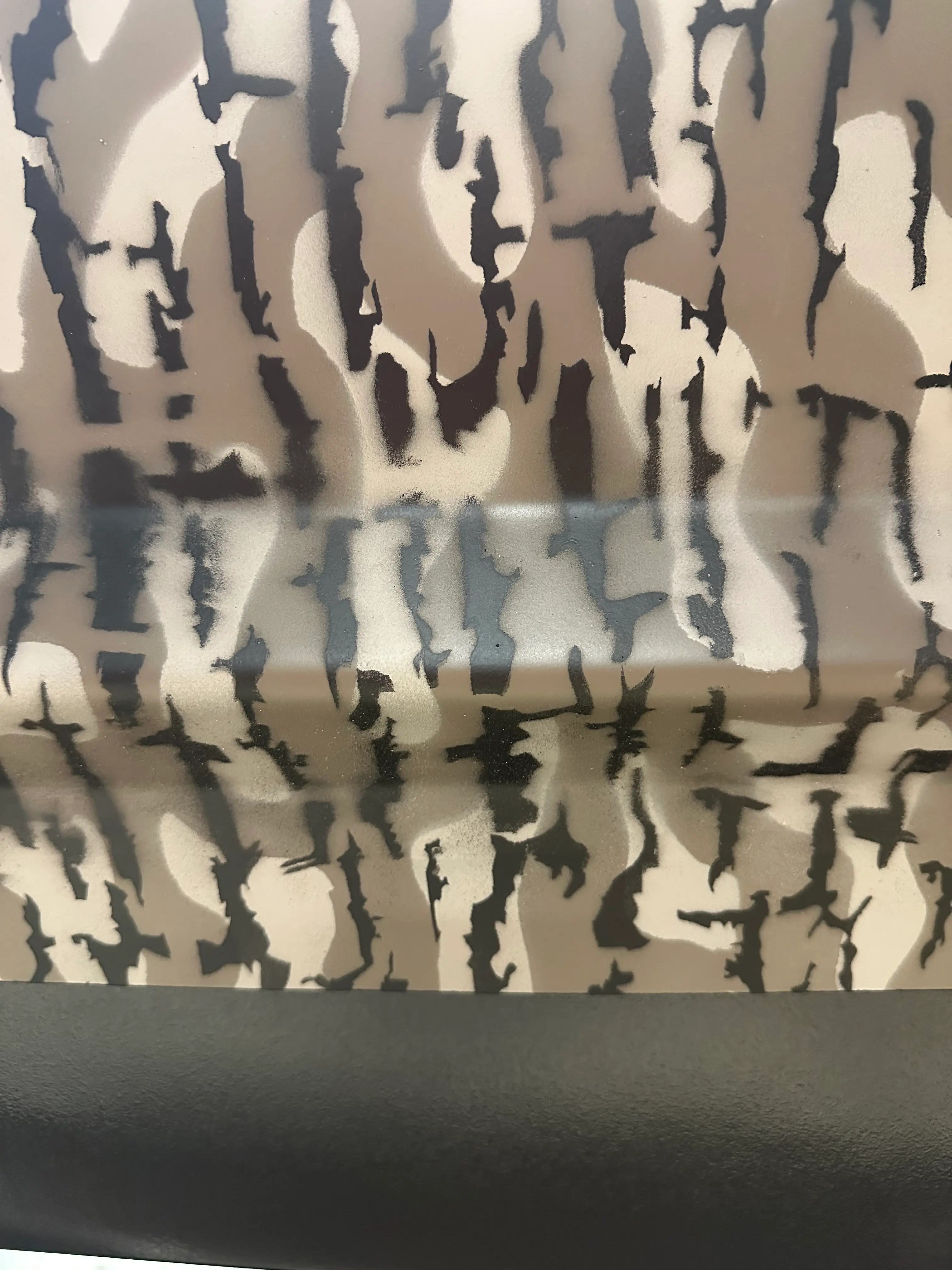 Close-up of fabric or material with a brown, beige, and black camouflage pattern above a smooth black surface.