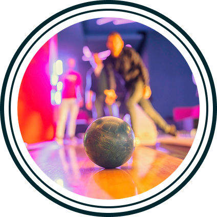 Bowling ball rolling on lane with blurred people and neon lights in the background.