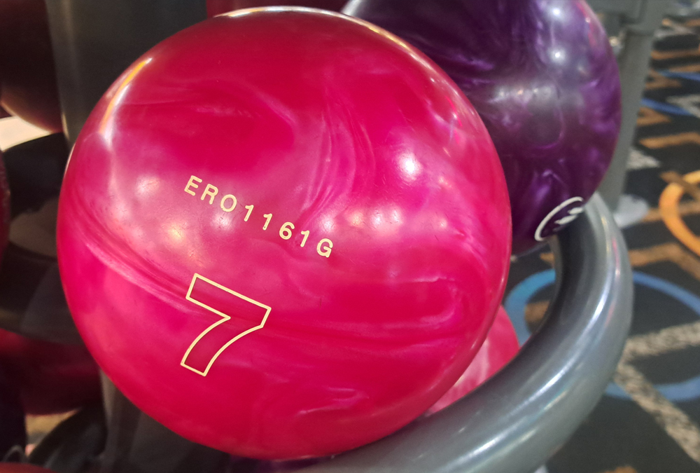 Close-up of a bright pink bowling ball numbered 7 with code ERO1161G on a ball rack.