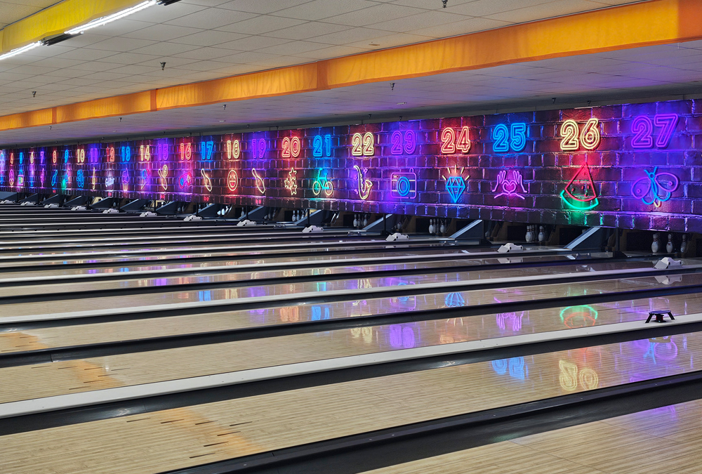 Empty bowling lanes with colorful neon numbers and symbols on a brick wall background.
