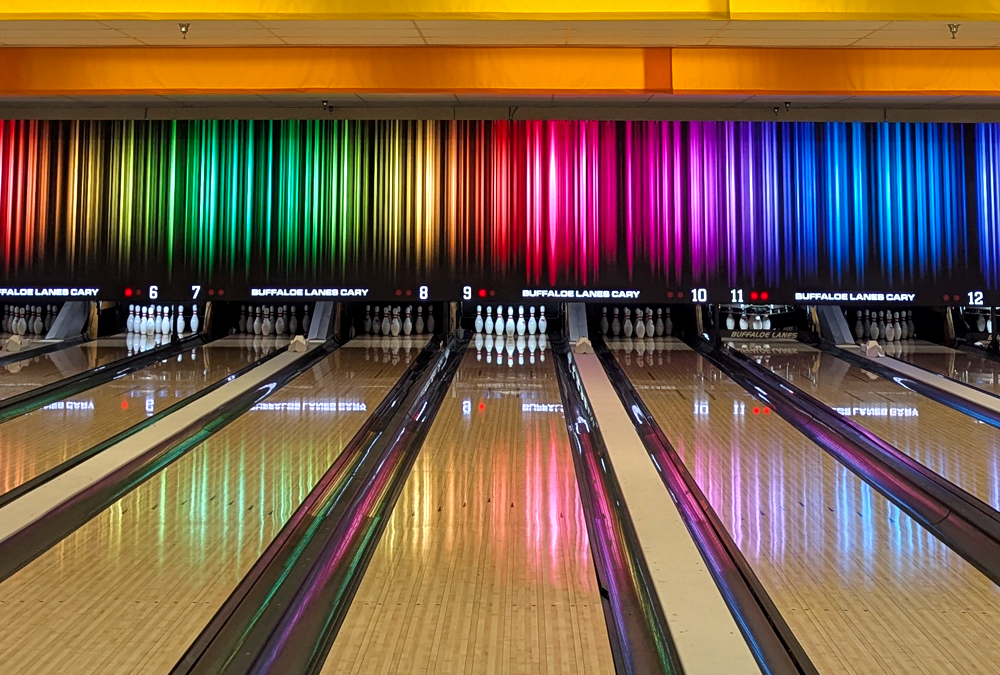 Bowling lanes with pins set and colorful vertical light stripes reflected on the shiny wooden floor.