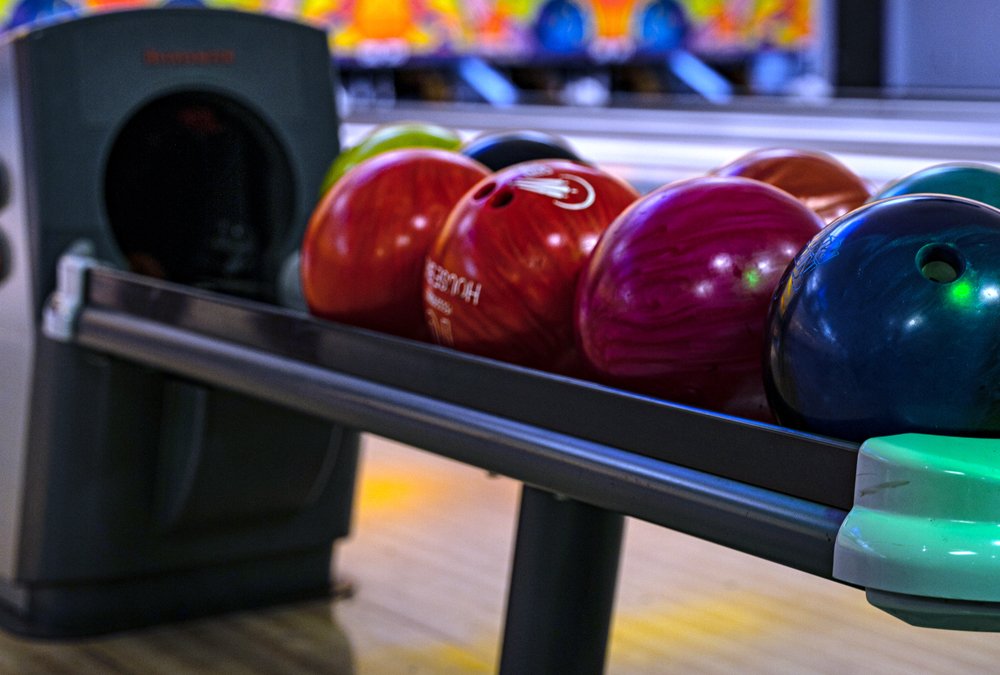 Colorful bowling balls lined up on a ball return rack at a bowling alley lane.