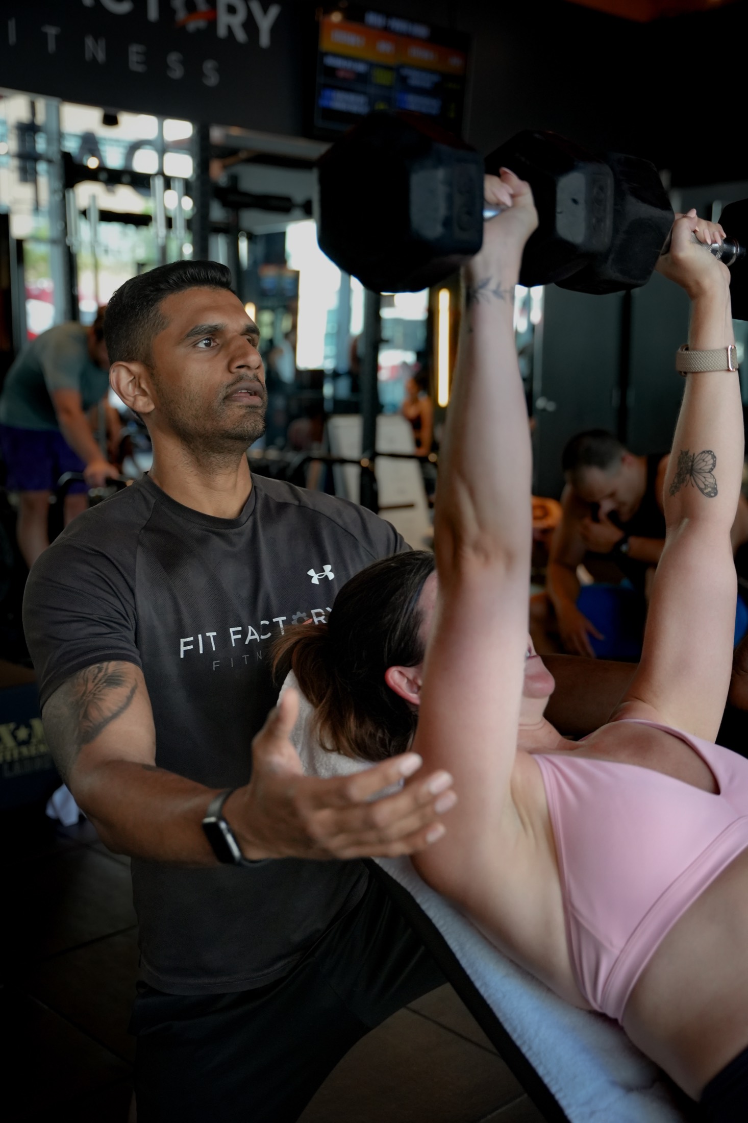 A Fit Factory coach spotting a member on the bench press